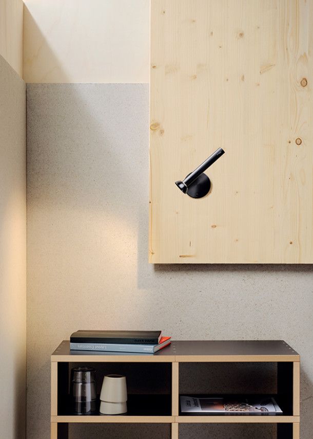 Nahaufnahme der schwarzen TOPOLED Wandleuchte von Baltensweiler, montiert auf einem Holzpaneel über einem Regal.