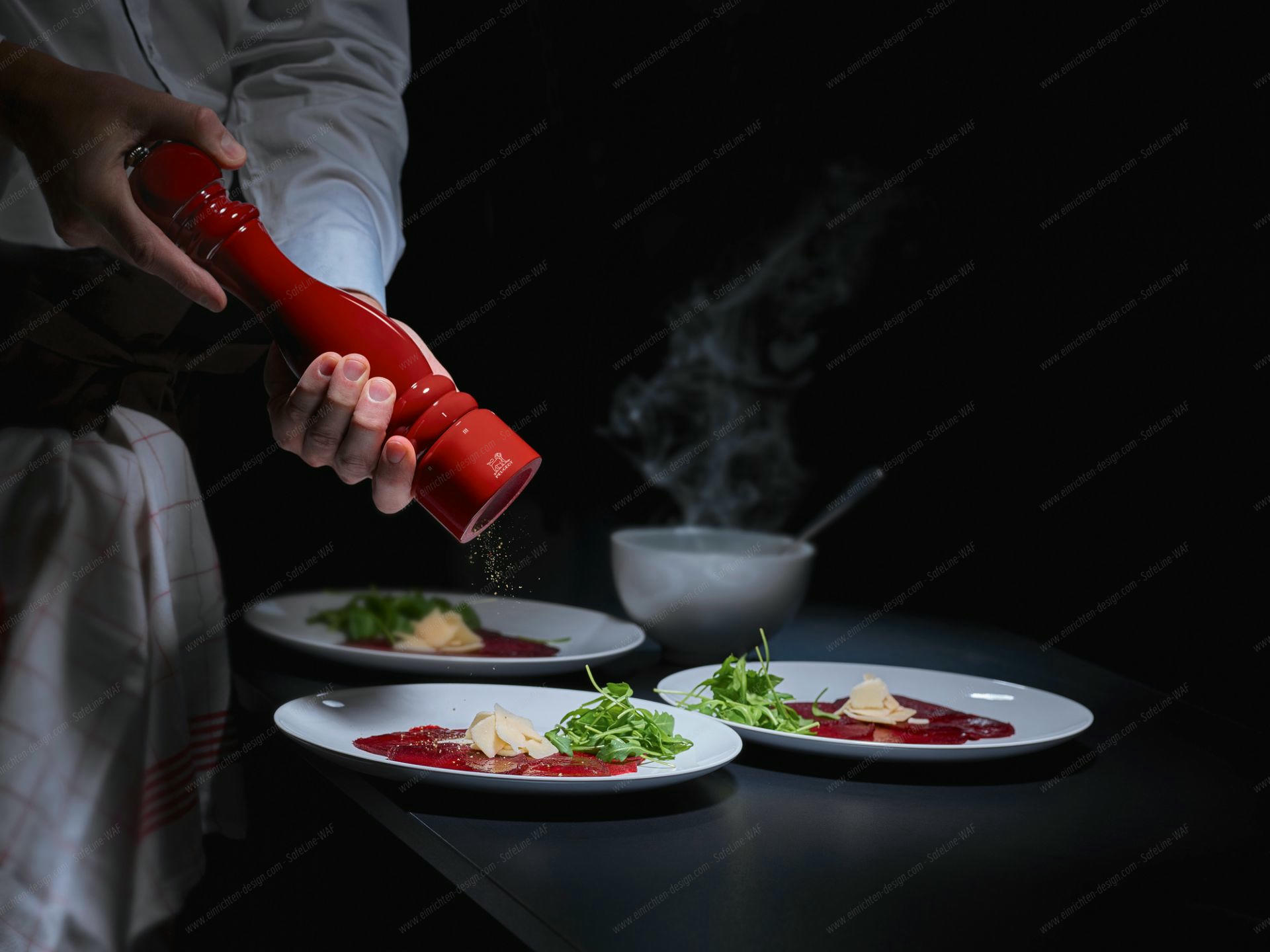 Rote Peugeot Salzmühle Paris 22cm in Aktion, würzt Carpaccio mit Rucola und Parmesan.