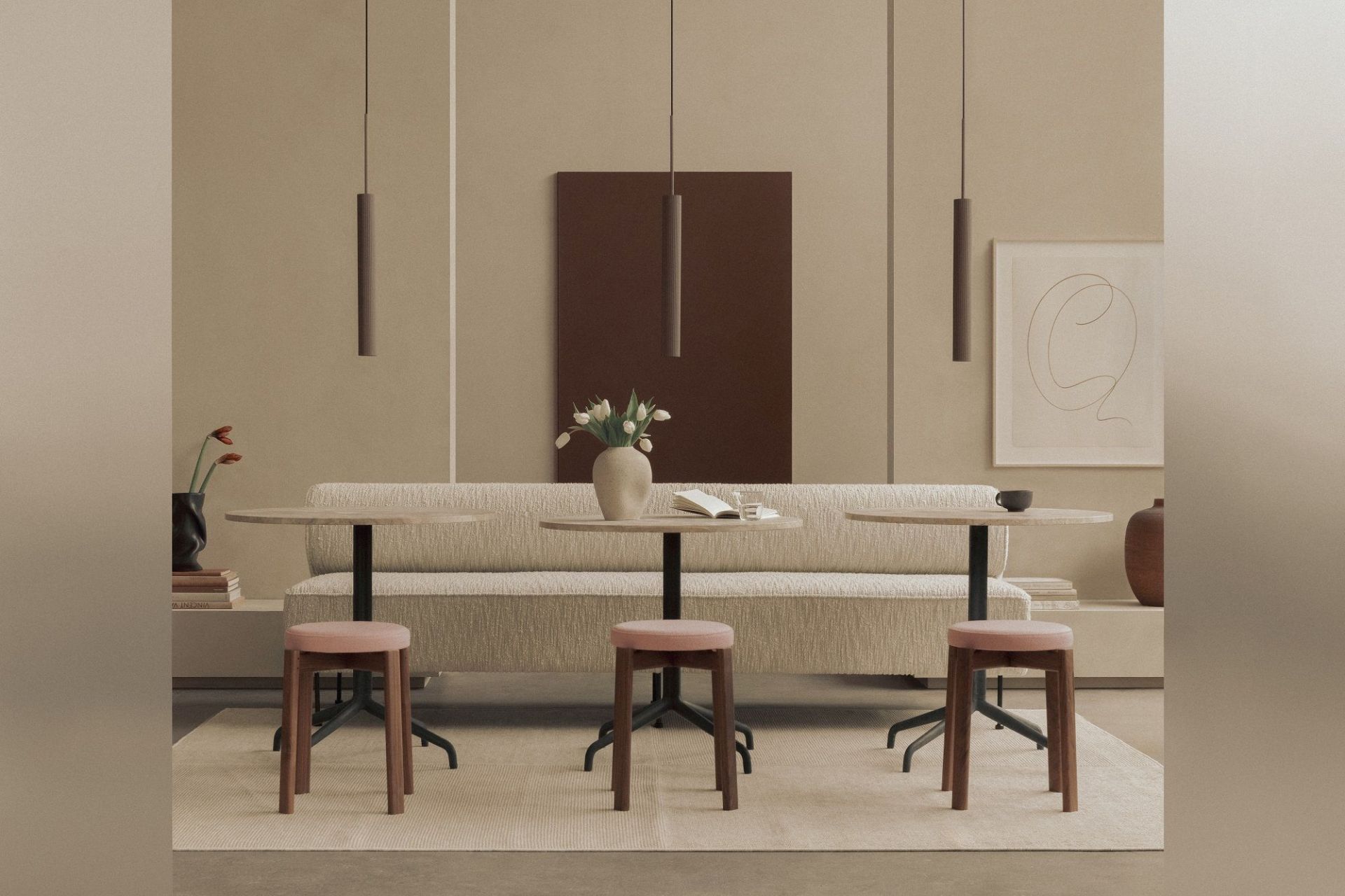 Nahaufnahme von drei Audo Copenhagen Passage Hockern mit rosa Sitzfläche und Holzkufen vor Tischen.