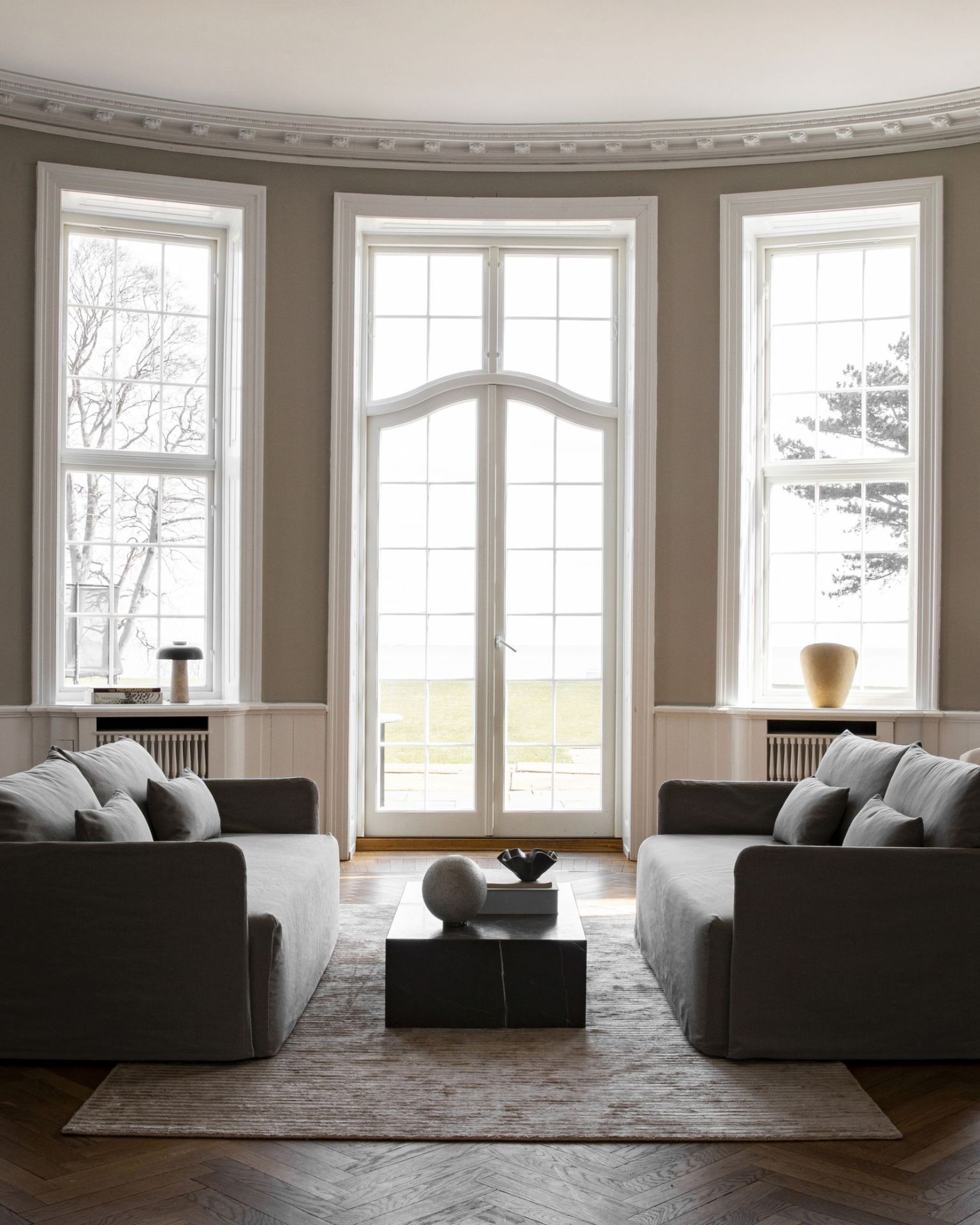 Helles Wohnzimmer mit zwei grauen Offset Sofas von Audo Copenhagen und einem dunklen Couchtisch.