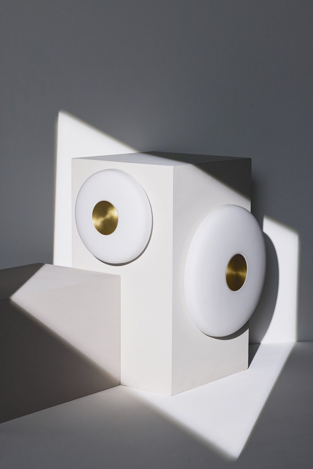 Nahaufnahme der Glint Glass Wandleuchte von Northern, opalweiß mit goldenem Akzent auf geometrischen Formen.