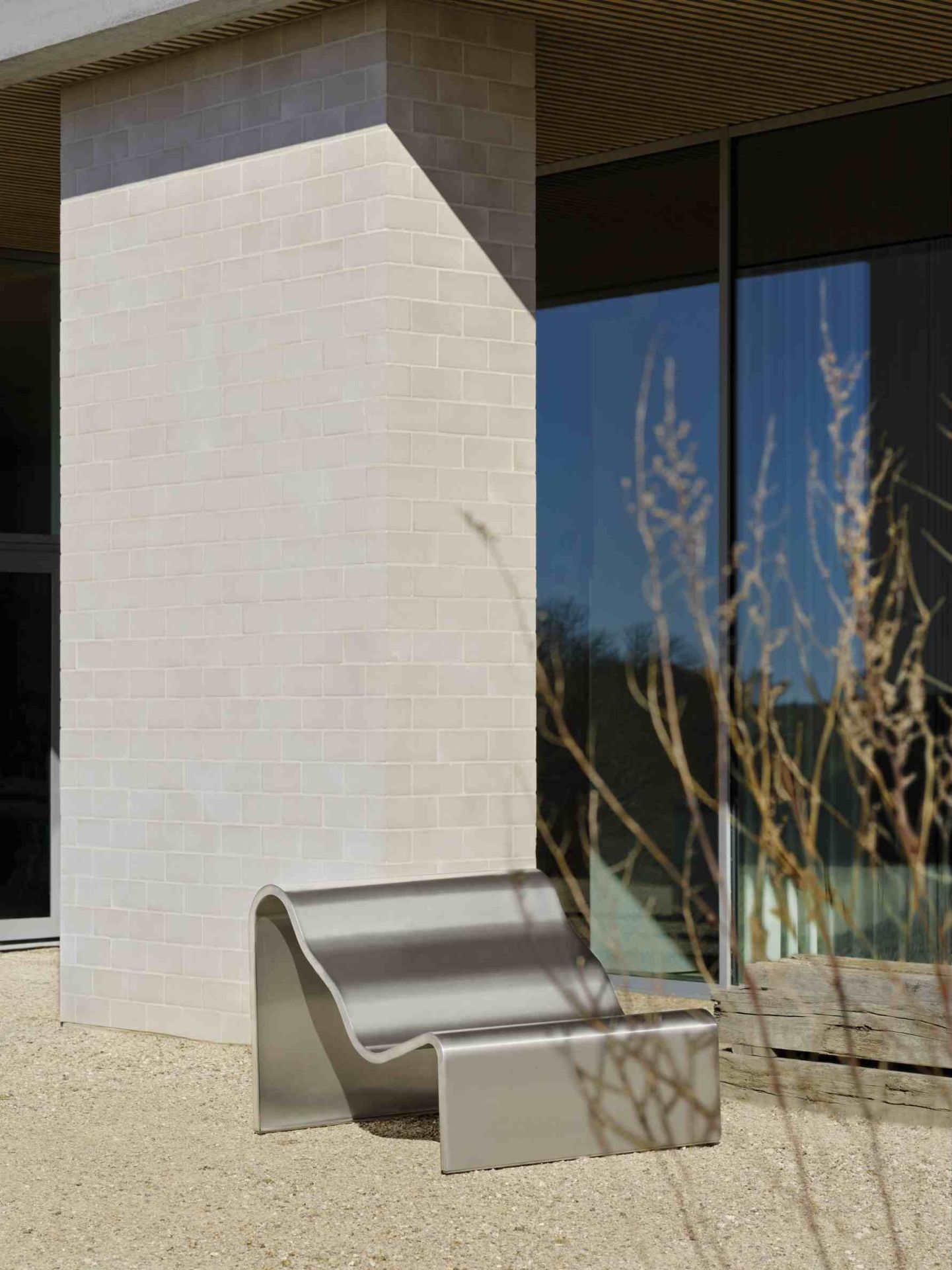 Muuto Dream Bench Outdoor Bank aus Edelstahl vor modernem Gebäude mit Fensterfront.