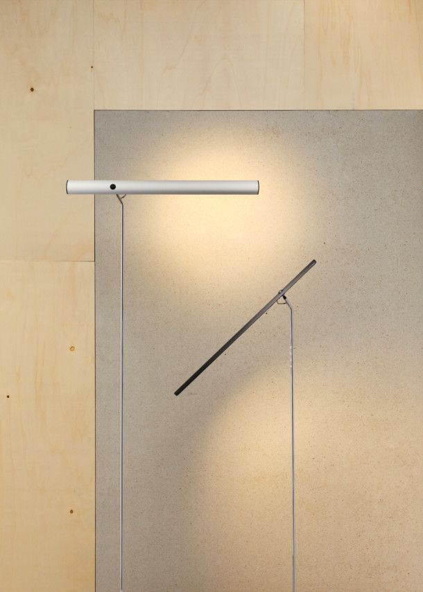 Zwei moderne LED-Stehleuchten in Silber und Schwarz vor einer Holz- und Betonwand.