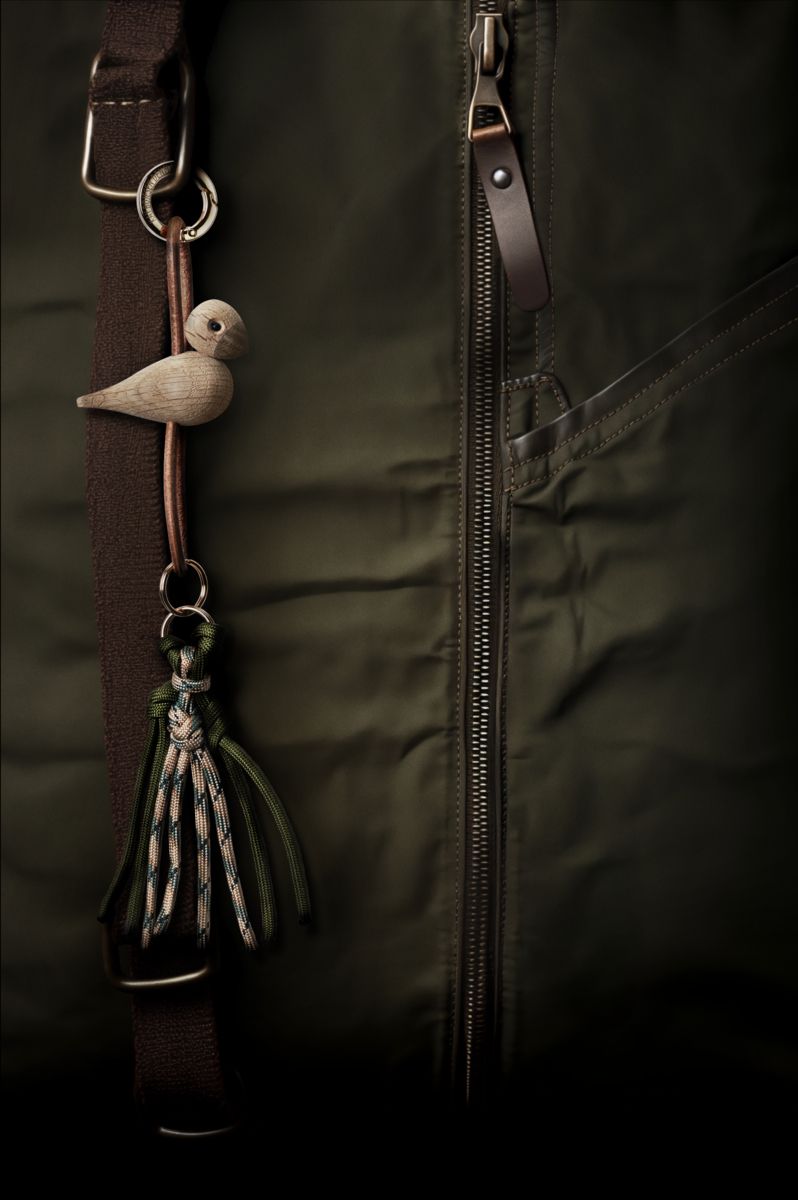 Kay Bojesen Vogel Schlüsselanhänger aus Eiche mit Lederband und dekorativer Quaste an einer Jacke.