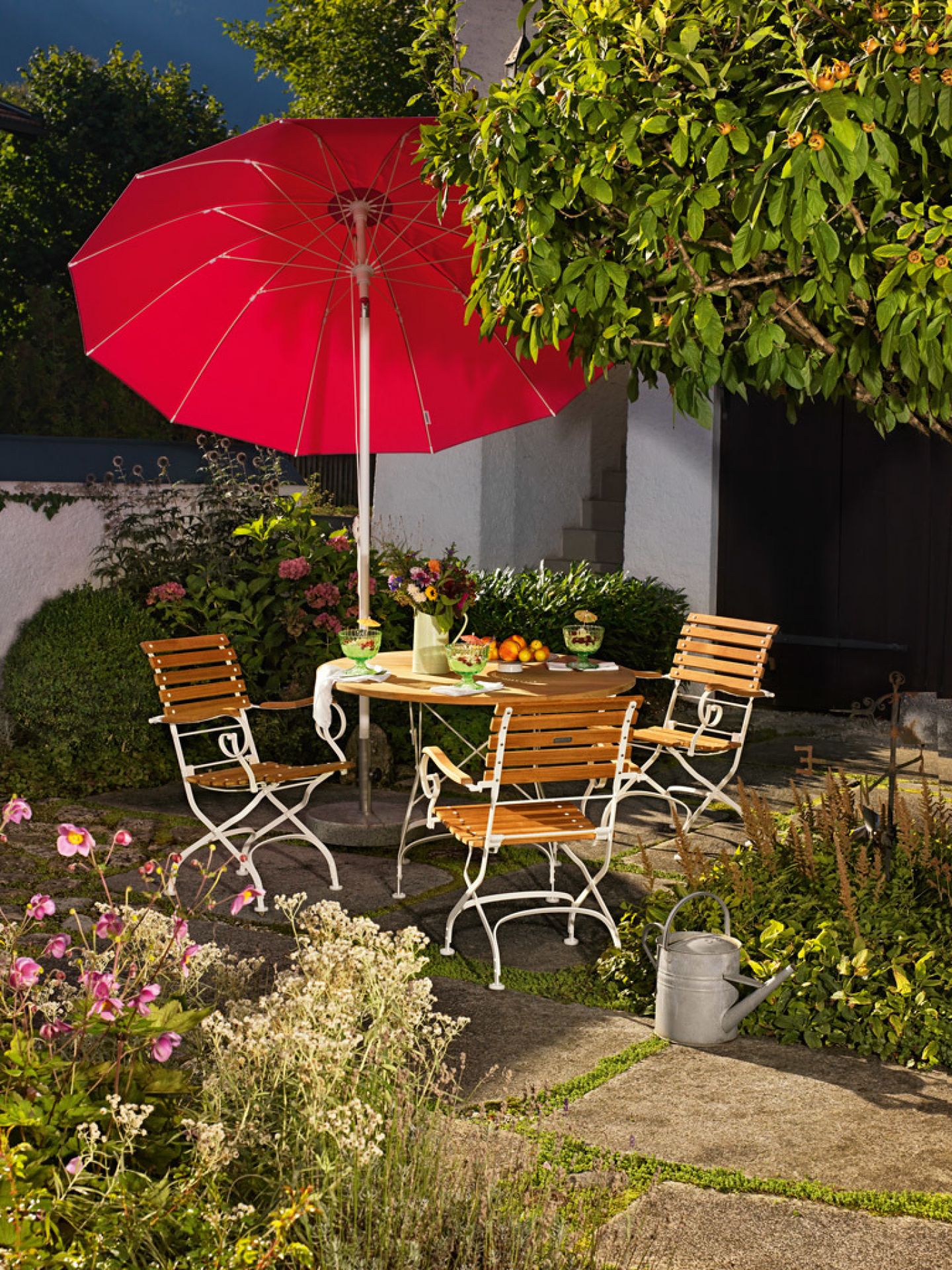 Weishäupl Classic Table klappbar Ø75 cm weiß mit Stühlen und rotem Sonnenschirm im Garten.