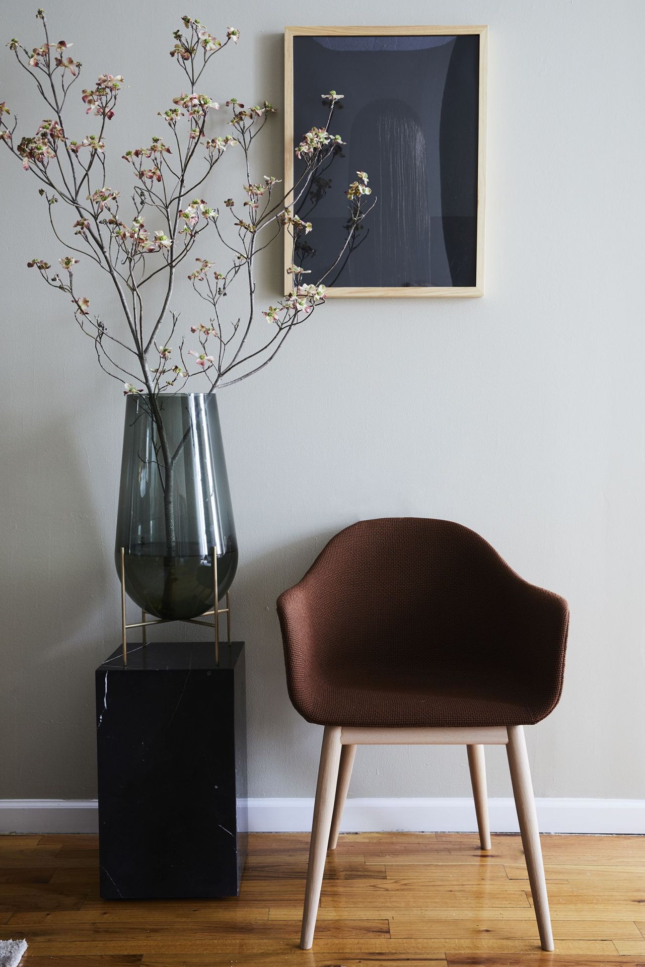 Brauner Audo Copenhagen Harbour Dining Chair Stuhl mit Holzbeinen neben Blumenvase und Kunstwerk.