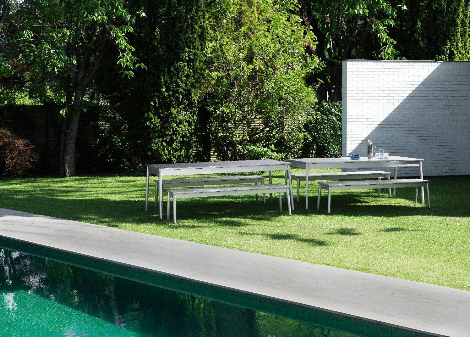 Normann Copenhagen Ex Tisch Outdoor mit Bänken im Garten neben Pool auf Rasenfläche, moderne Gartenmöbel.