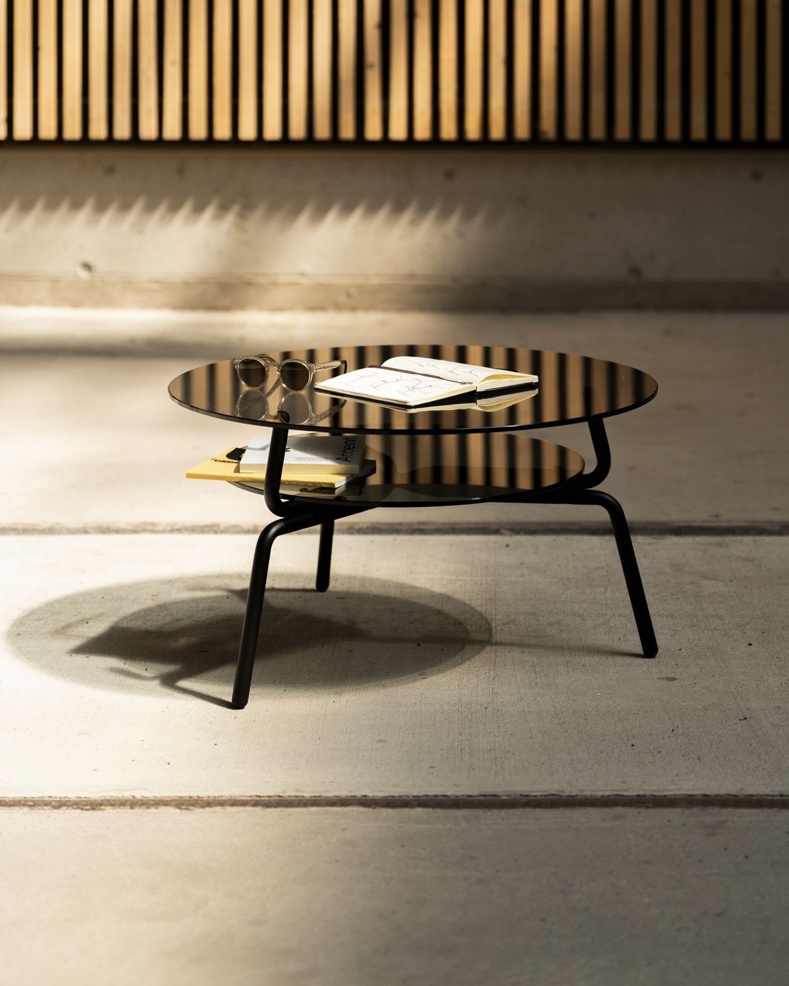 Lej Couchtisch Transparent Mox mit runder Glasplatte und schwarzem Metallgestell, mit Ablagefläche.