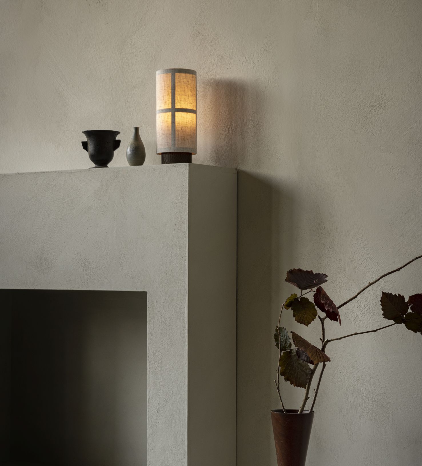 Audo Copenhagen Hashira Tischleuchte aus Stoff, mit stimmungsvollem Licht neben Vasen auf Regal.