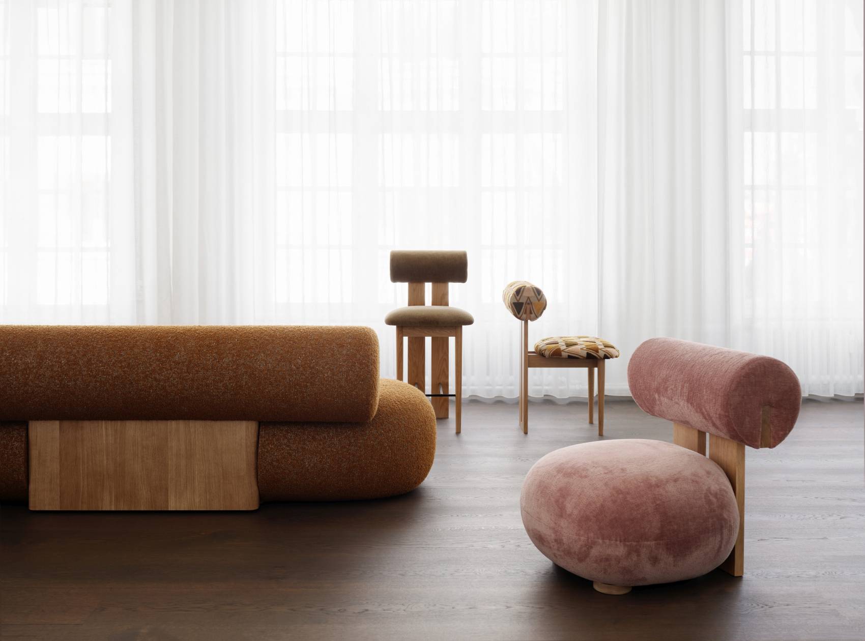 NORR11 Hippo Lounge Chair Sessel in Rosa und Braun mit passenden Stühlen vor Vorhang.