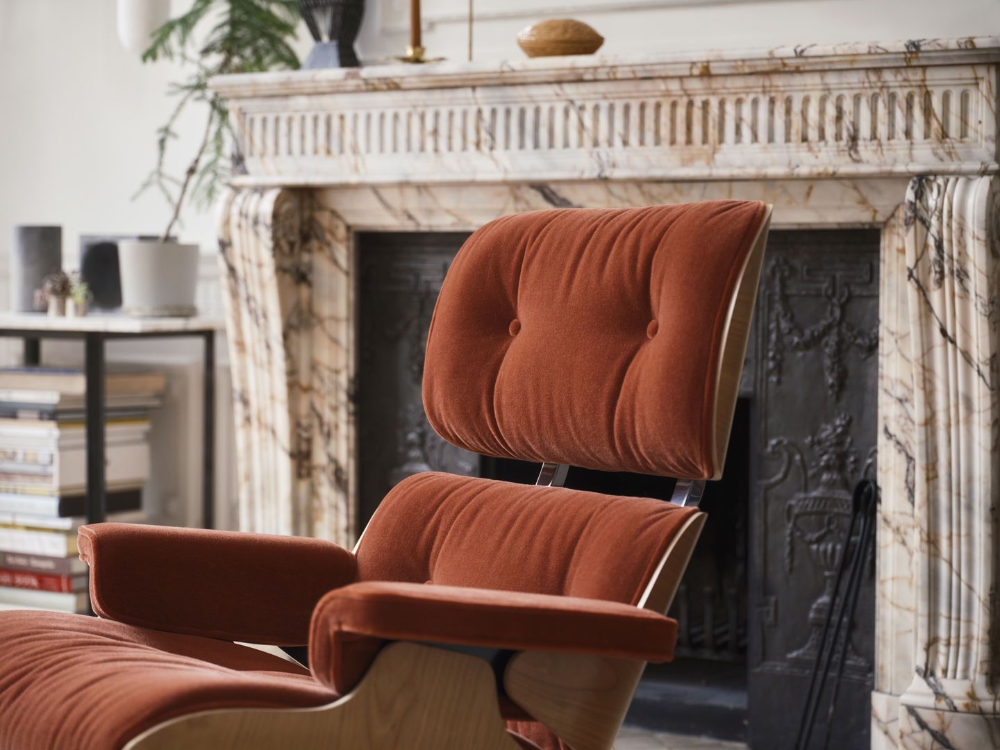 Detailaufnahme des Eames Lounge Chair Sessels von Vitra in braunem Stoff vor einem Kamin.