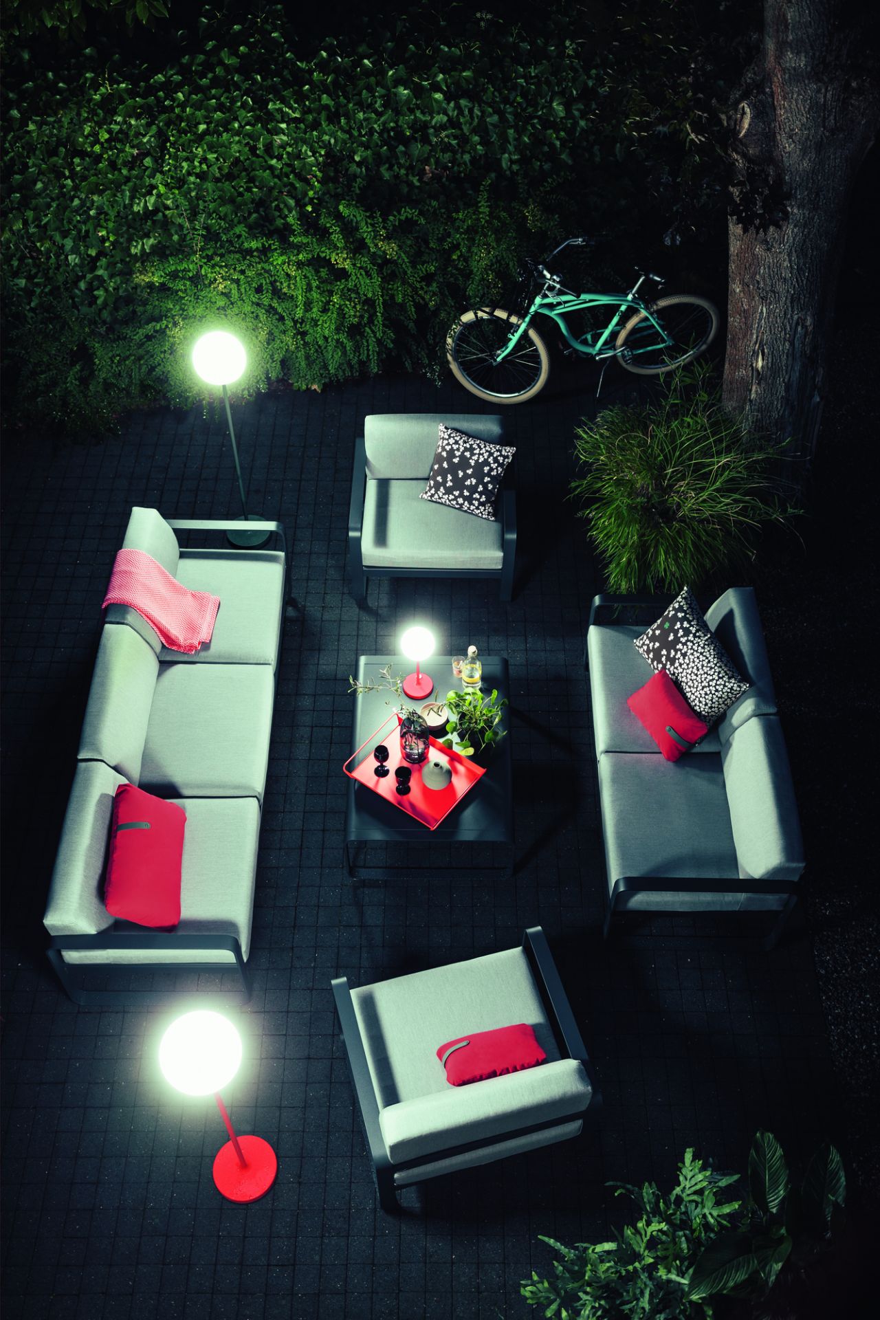 Anthrazitfarbene Mooon! Stehleuchte von Fermob beleuchtet eine moderne Outdoor-Lounge mit Gartenmöbeln und Dekoration.