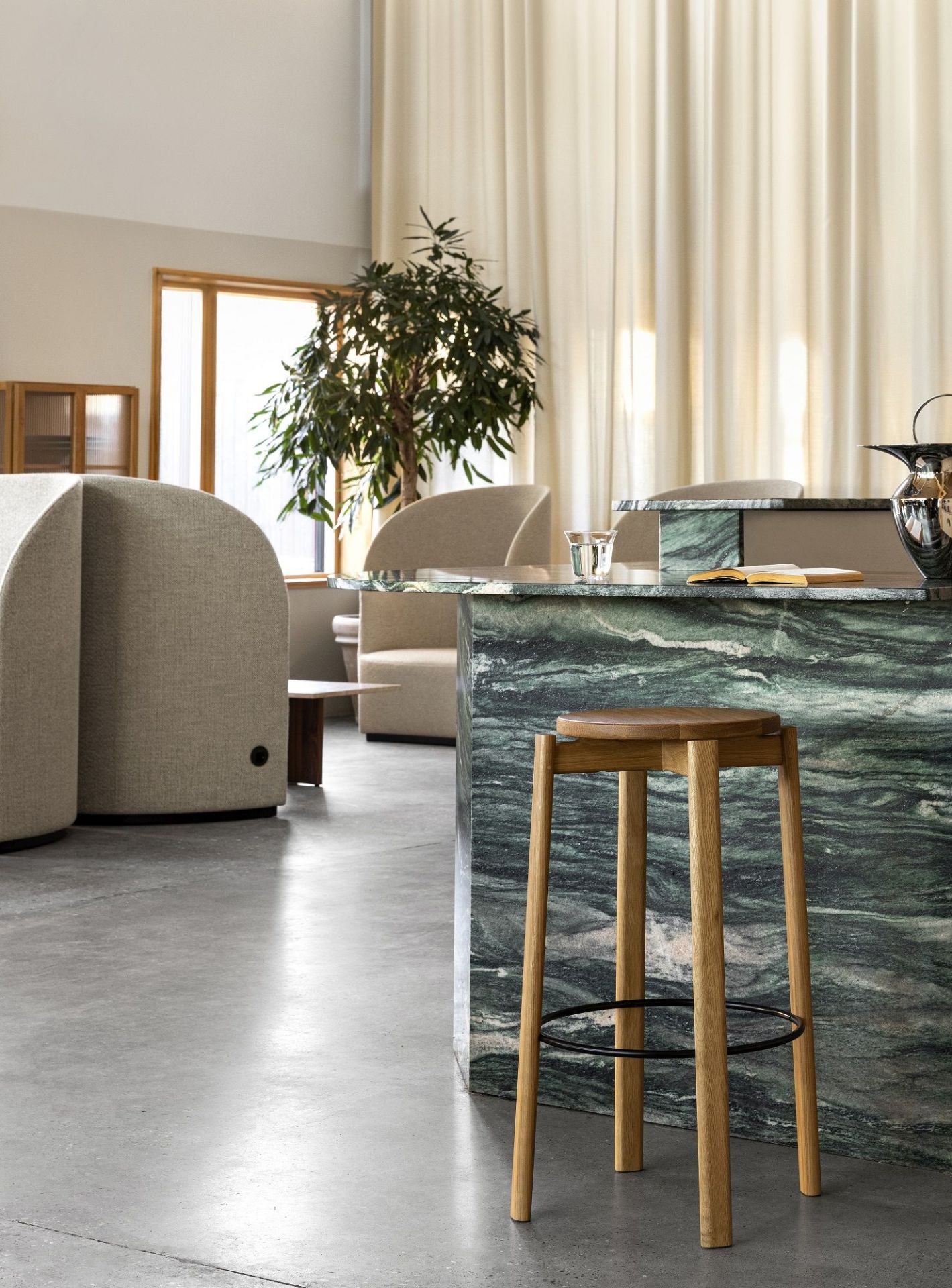 Audo Copenhagen Passage Bar Stool aus Eichenholz vor einer grünen Marmor-Bar in modernem Interieur.