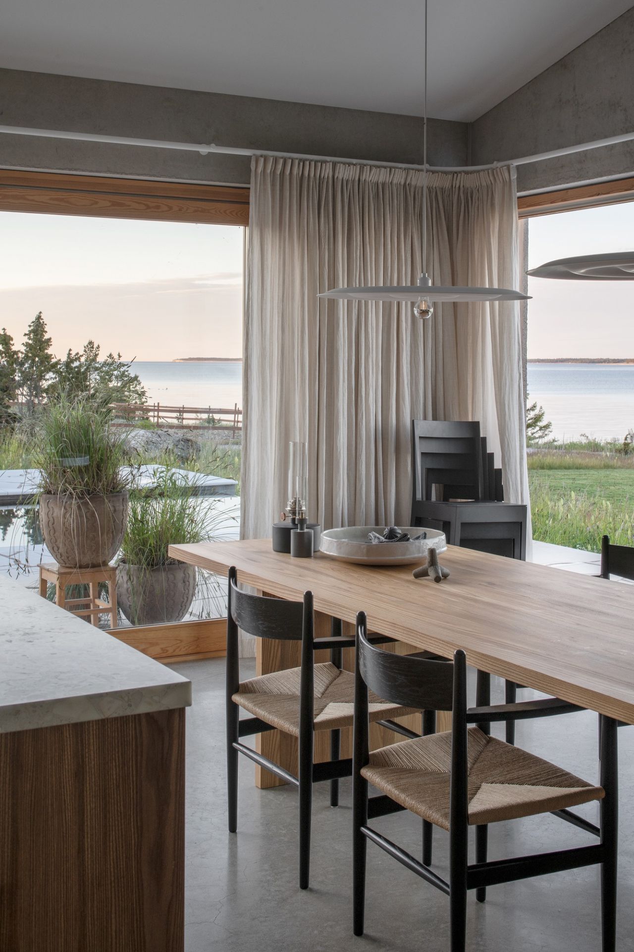 Helle wästberg w171 Alma Pendelleuchte über Esstisch mit Stühlen in modernem Esszimmer mit Meerblick.