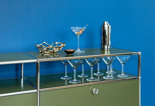 USM Haller Lowboard in Olivgrün mit Klapptüren, stilvolles Möbelstück mit Gläsern und Bar-Zubehör dekoriert.